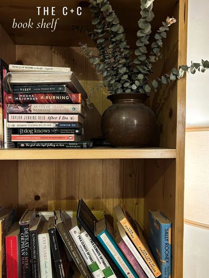 A stack of books on our shelf, including titles like "A Burning" and "An Orchestra of Minorities". We aim to offer a diverse range of voices and stories.