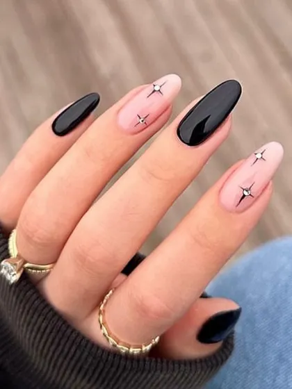 A chic and minimalist design with black starbursts on a nude accent nail, paired with solid black almond nails.