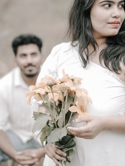 A beautiful portrait with the bride in focus holding flowers, and the groom looking on from the background.