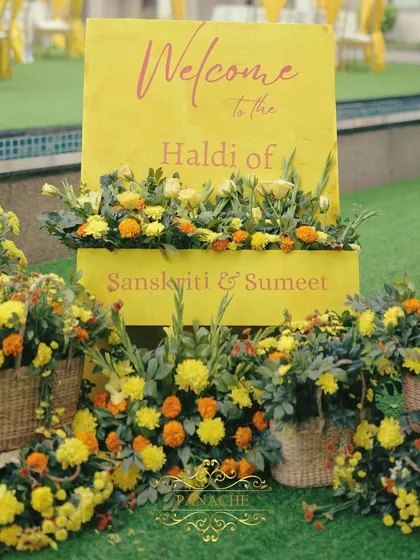 A close-up of the Haldi welcome sign, showing the vibrant yellow color and the beautiful arrangement of fresh flowers.