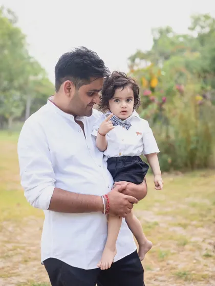 A father holds his young son, who is dressed smartly in a bow tie. This portrait captures a sweet, gentle moment between father and son during their family outdoor shoot.