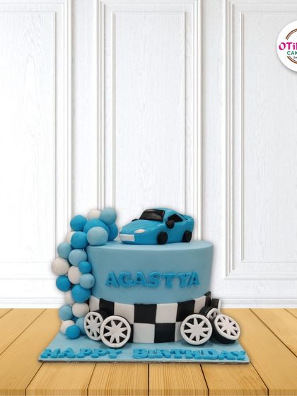 A cool car-themed cake for a little racer. This design features a hand-sculpted blue fondant car, a checkered flag pattern, and a cascade of blue and white balloon-like spheres.