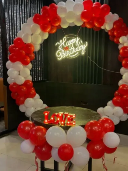 A romantic red and white balloon ring setup. This decoration is perfect for an anniversary or a birthday, featuring a 'Happy Birthday' neon sign and a 'LOVE' marquee sign.