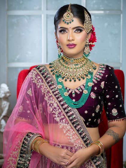 This bridal portrait highlights the beauty of contrast, pairing a deep velvet lehenga with striking emerald green jewelry. The makeup features a sharp wing and a bold lip to complete the powerful look.