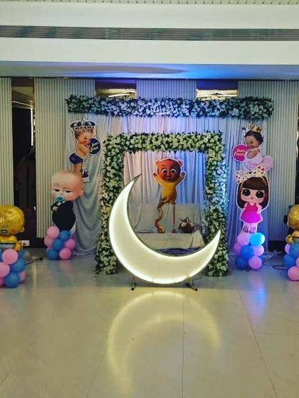 A 'Boss Baby' themed naming ceremony decoration with a lighted moon prop. The setup uses character cutouts and balloons to create a fun and stylish look.