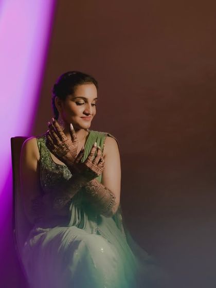 The bride admires her henna-adorned hands in this creative portrait, with soft lighting and a purple flare creating a dreamy atmosphere.