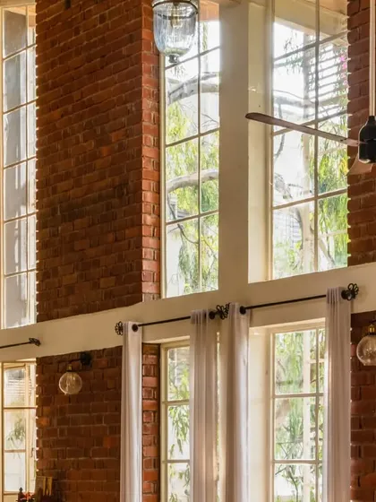 The double-height windows at The Brick Loft flood the space with natural light. The exposed brickwork and sleek window frames create a beautiful contrast, while the greenery adds to the cozy, inviting atmosphere.