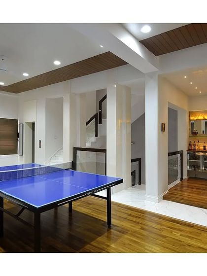 A multi-functional entertainment space featuring a table tennis table and an adjacent home bar. The warm wood floors and backlit onyx bar create a welcoming area for games and socializing.