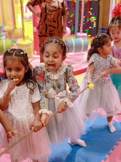 Little girls in party dresses play a game of tug-of-war. We believe in mixing active games with our themed decor for a well-rounded party experience.
