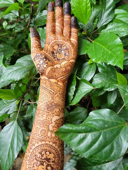 A look at a fully completed bridal henna design with eye-catching mandalas and flowing patterns. The dark fingertips and detailed work create a classic and rich look for any bride.