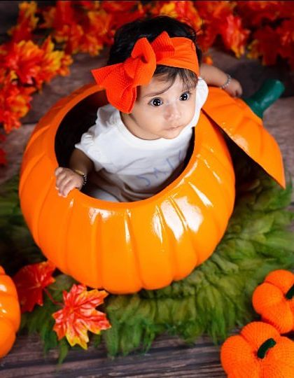 An aerial view of a baby peeking out of a pumpkin, a creative and cute shot for an autumn-themed session.