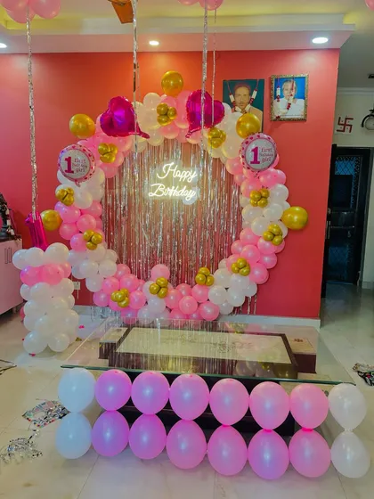 A sweet first birthday setup with a circular balloon arch in pink and white, a shimmer backdrop, and a neon sign.