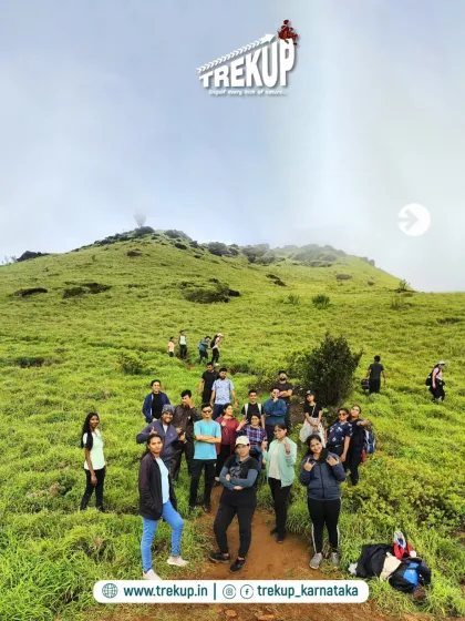 A group of trekkers posing on the trail at Bandaje, with the rolling green hills and misty peak behind them.