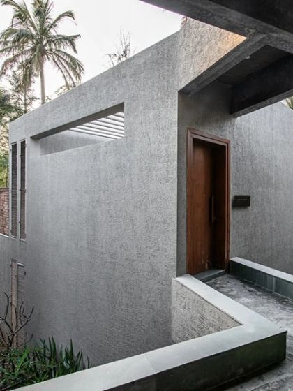 The entrance to a room at the Anahaspa retreat, where minimalist concrete forms are softened by the surrounding greenery and warm wooden doors.