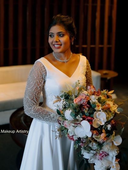 A stunning Christian bride holding her bouquet. Her makeup is elegant and understated, with a focus on flawless skin and a soft smile.