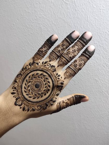 A detailed mandala design with a leafy wreath at its center. The fingers are adorned with intricate patterns, and the overall look is very full and traditional.