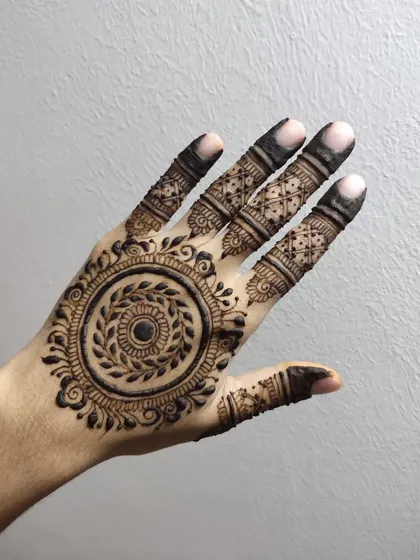 A detailed mandala design with a leafy wreath at its center. The fingers are adorned with intricate patterns, and the overall look is very full and traditional.