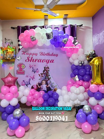Shravya's butterfly-themed first birthday. This home setup features a round photo backdrop and a balloon arrangement in purple, pink, and white.