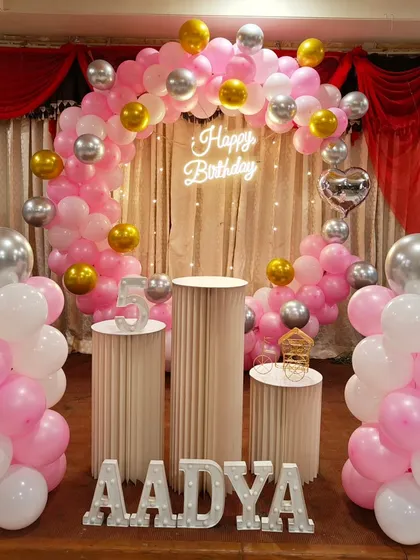 An elegant and classic birthday setup using a pink, white, and silver color scheme. This design features a beautiful balloon arch, a neon 'Happy Birthday' sign, and stylish white pedestals, showing that a party can be sophisticated without a specific character theme.