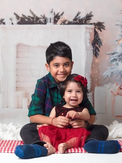 A happy sibling portrait from a Christmas mini session. The festive setup with a tree and fireplace creates a cozy and magical holiday memory.