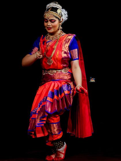 A full-length portrait of a dancer in traditional costume against a black backdrop, highlighting the elegance of her stance.