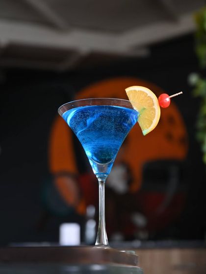 A striking blue cocktail in a martini glass, garnished with an orange slice and a cherry. This drink is a real head-turner.