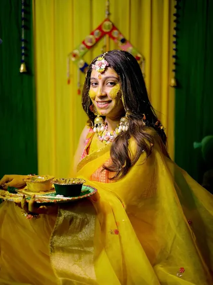 The bride, glowing in yellow, holds a thali during her Haldi ceremony, ready for the rituals to begin.