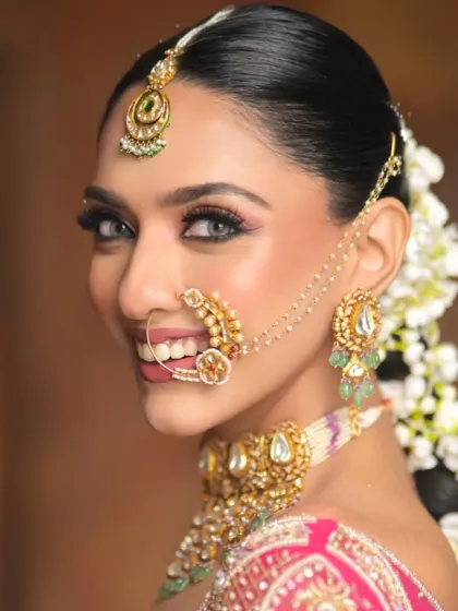 A close-up portrait highlighting the front of the hairstyle, with a clean side part and hair tucked neatly behind the ears, allowing the focus to remain on the makeup and the start of the gajra braid.