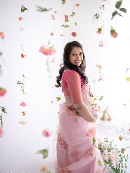 A lovely, bright portrait of the mom-to-be. She looks directly at the camera with a warm smile, surrounded by a backdrop of soft, floating flowers.