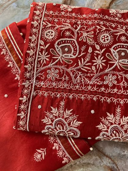 A close-up of the intricate floral and paisley embroidery on the red silk chanderi fabric.