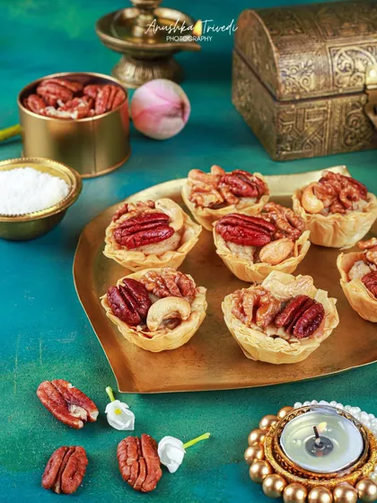 Mini nut tartlets on a brass plate, styled with a diya for Diwali. The rich colours and traditional props create a beautiful and authentic festive scene.