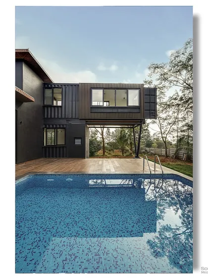 The cantilevered section of the container home appears to float above the swimming pool. This architectural shot captures the reflection of the building in the water, creating a stunning, symmetrical image.