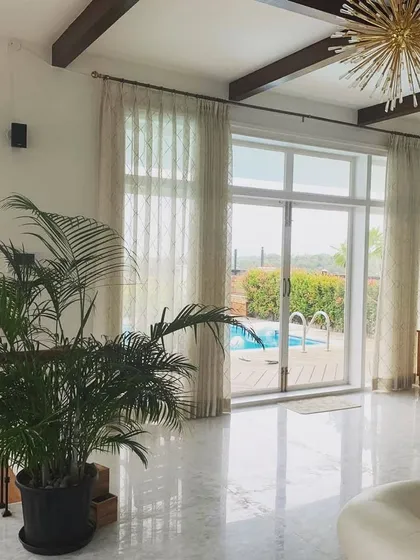 This living space in a Mysore residence for a doctor exemplifies our tropical modernism style. Large glass doors open directly onto a terrace with a swimming pool, creating a seamless flow between the indoor and outdoor areas, complemented by marble floors and natural light.