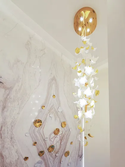 A close-up of the cascading chandelier, which is made of custom white and gold elements. It hangs through the double-height space, illuminating the staircase and the feature wall.