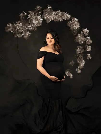 A dramatic and elegant portrait in a black off-shoulder gown. The flowing fabric and silver floral hoop create a sophisticated and moody atmosphere.