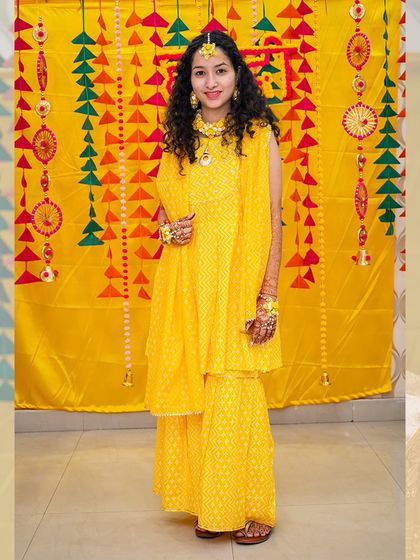 A full-length portrait of the bride in her beautiful yellow sharara, ready for her haldi ceremony.
