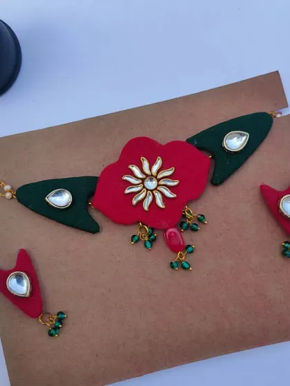 This choker set features a large red fabric flower with a Kundan center, flanked by green fabric pieces. It's a bold and beautiful choice for a bride or wedding guest.