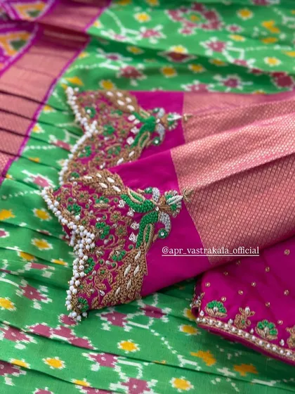 An exquisite peacock motif embroidered on the sleeve of a pink blouse, using green thread and pearl details, set against a green ikat saree.