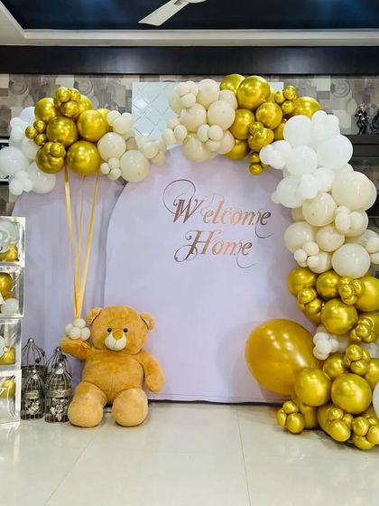 An elegant "Welcome Home" setup in white and gold, with a large teddy bear and "BABY" blocks.
