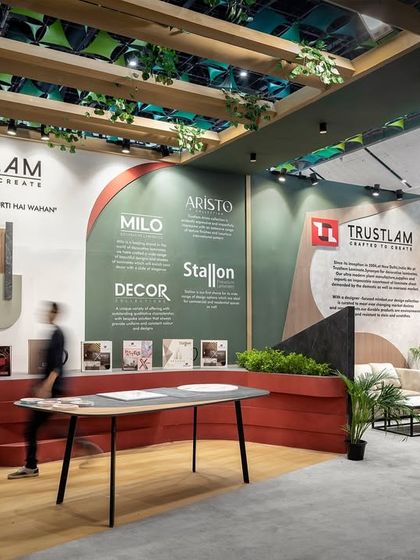 The Trustlam exhibition stall was designed to feel like a tribal sanctuary, using primitive forms and natural materials. This reception area features a curved counter and layered wall panels that showcase the brand's laminate products.