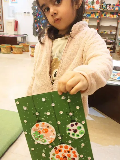 This little one is holding up her lovely green Christmas card, decorated with sparkly, fingerprint-stamped ornaments.