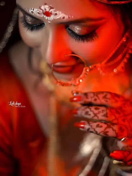 A detailed close-up of the bride's face, focusing on her intricate henna and nath. The dramatic red lighting adds a touch of romance and intensity.