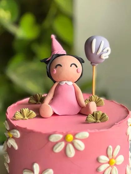 A close-up of the adorable custom fondant doll topper for the half-birthday cake, complete with a party hat and a mini balloon.