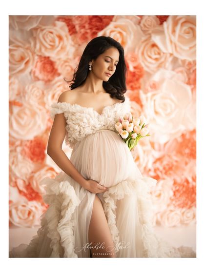 A quiet, contemplative moment against the stunning flower wall, with the mother-to-be looking down at her bouquet.