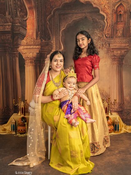 A beautiful portrait of a mother with her two children, all dressed for a Janmashtami celebration. The baby as Krishna and the older sister in traditional attire make a lovely trio.