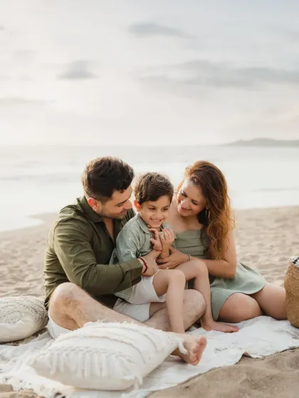 A family cuddles together on a blanket at the beach. The soft sunset light and their happy expressions create a warm and loving family portrait.