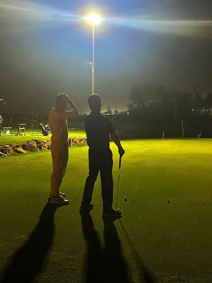 Two players discuss strategy on the putting green under the bright floodlights. The game doesn't stop when it gets dark here.