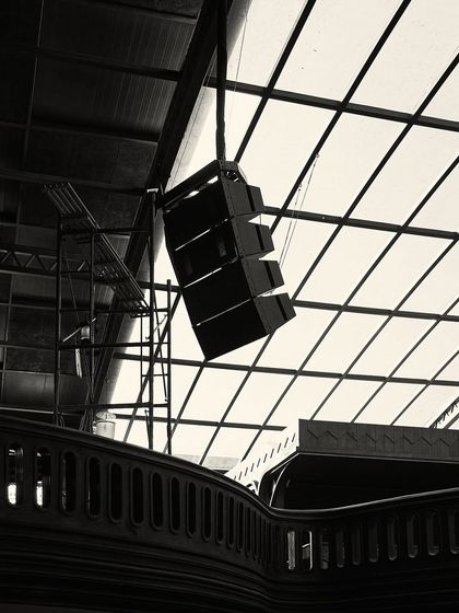 An upward-looking shot that captures the juxtaposition of the classic wooden balcony, the modern sound system, and the light-filled glass canopy.