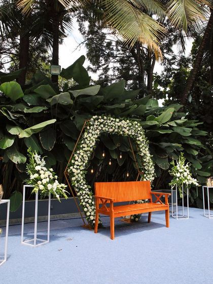 A hexagonal arch decorated with white flowers and greenery, set up on a blue carpeted stage. This shows another option for a clean and modern ceremony backdrop.