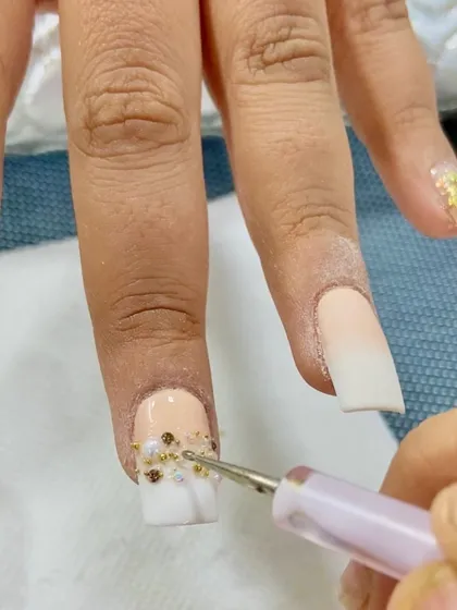 A close-up look at creating detailed pearl nail art. I'm carefully placing tiny pearl and gold bead accents onto an ombré nail, building a textured and luxurious design perfect for a bride.